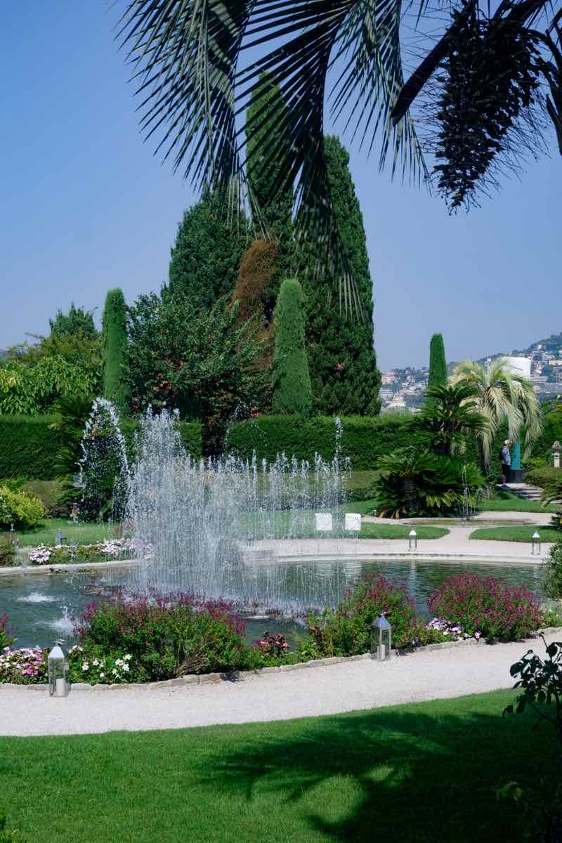 A fountain in a garden of clipped hedges and palm trees